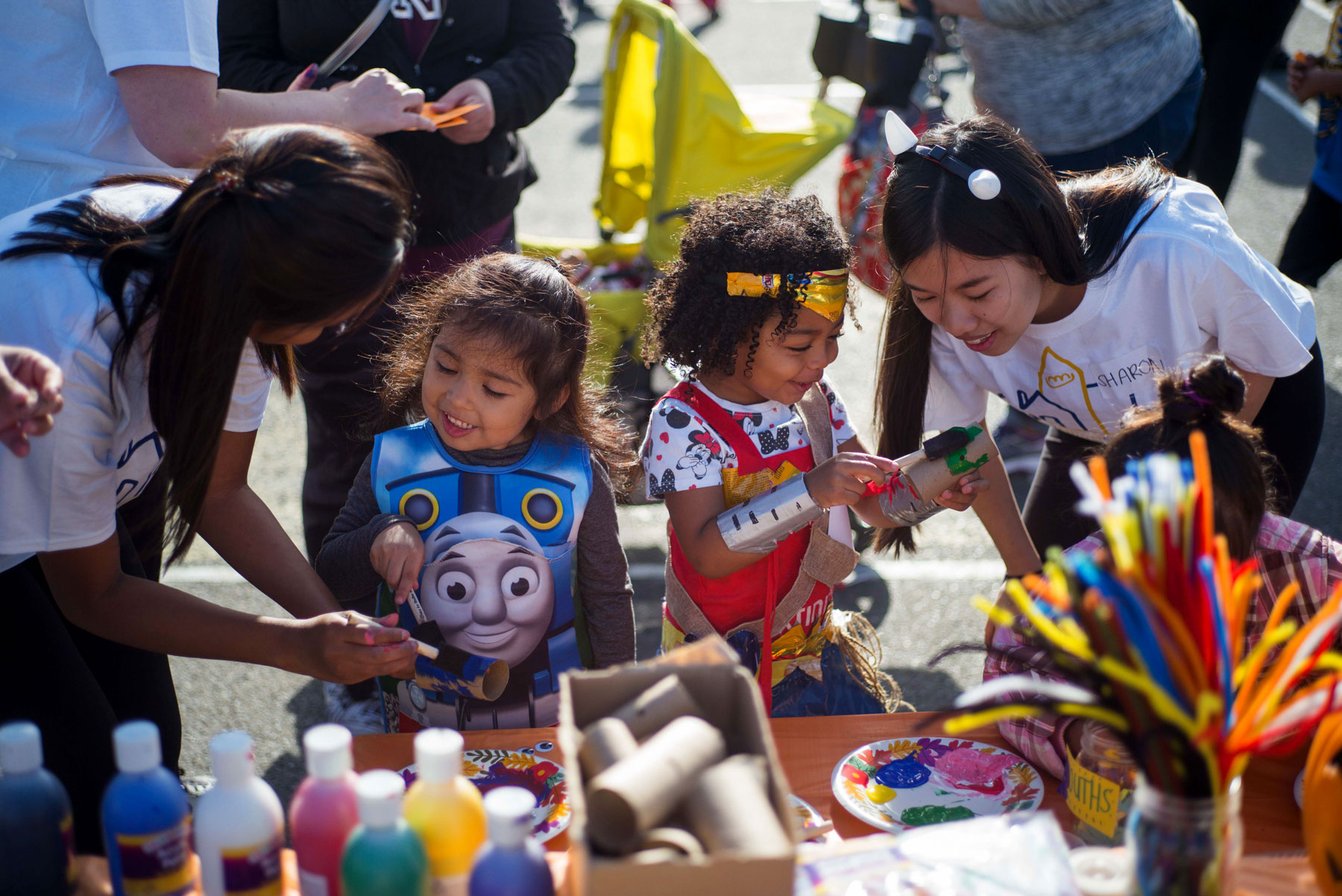 Student volunteers help two kids with their arts and crafts during a halloween event.