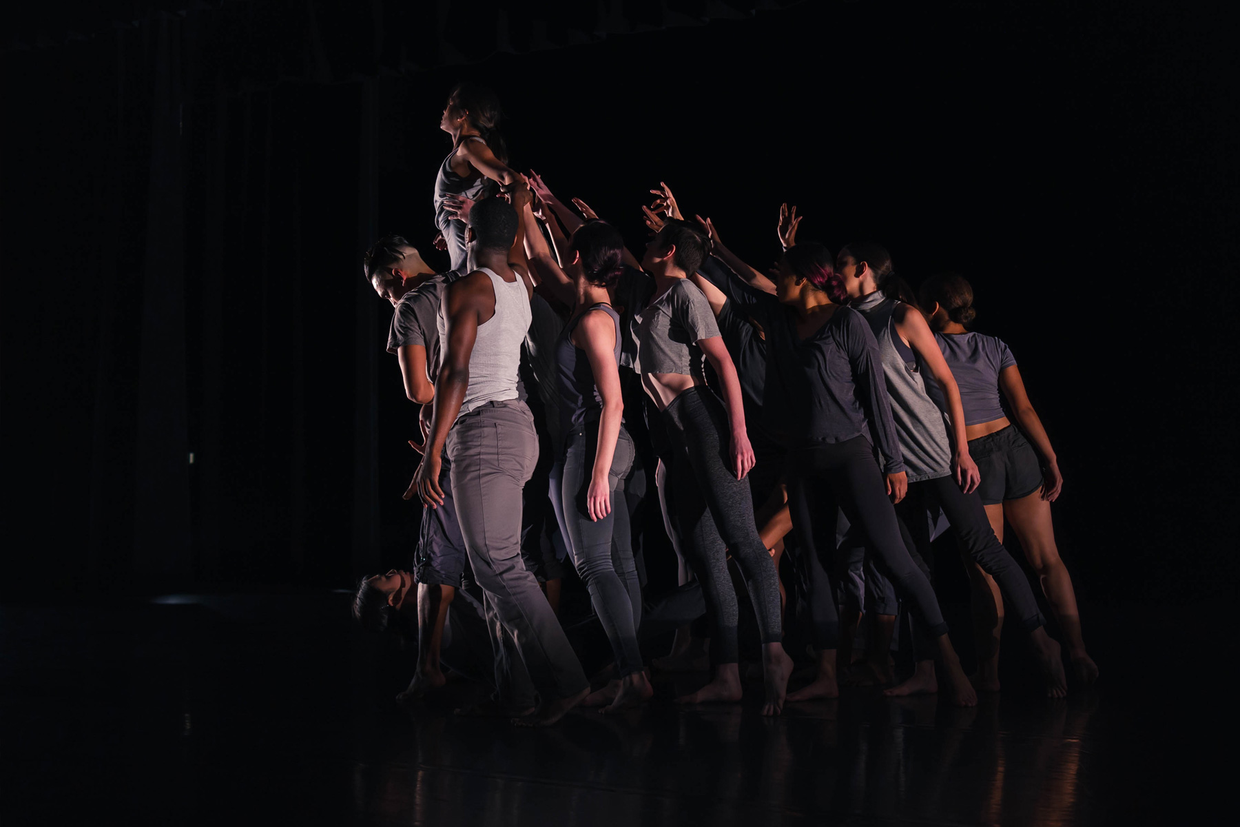 Dance students under a bright spotlight in a dark stadium pose tightly together on stage.