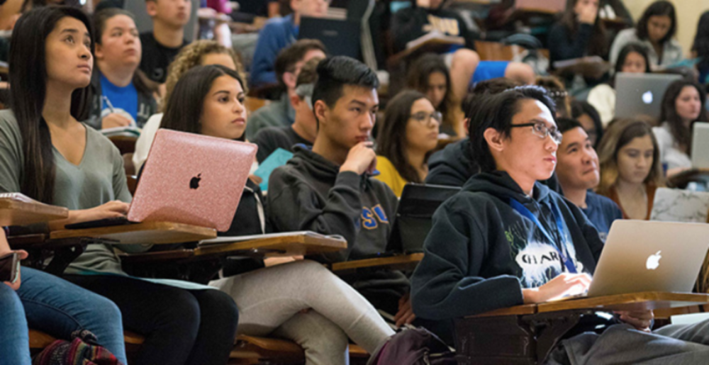 Students in classroom taking notes on laptops and notebooks