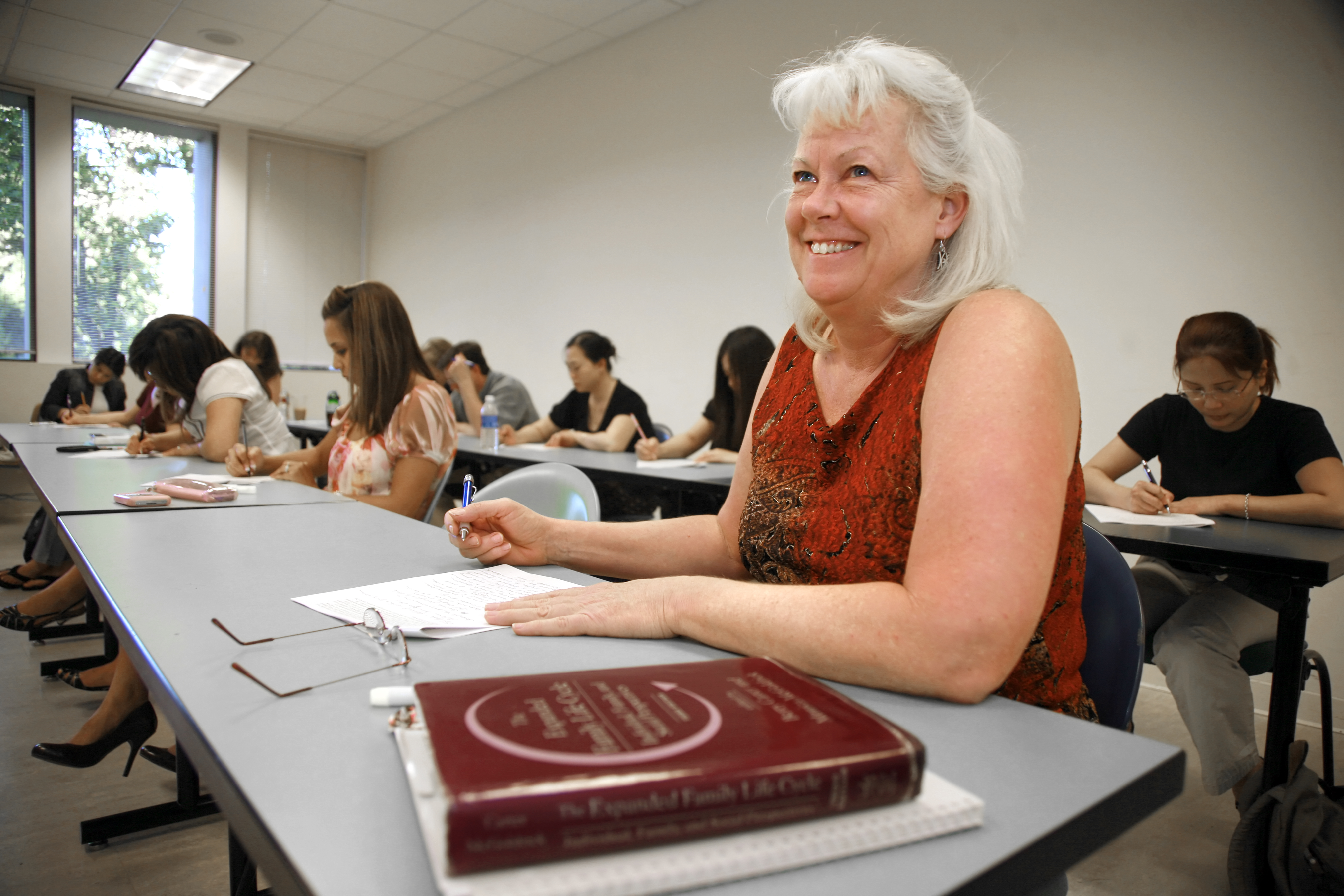 A middle-age woman sitting by the classroom desk.