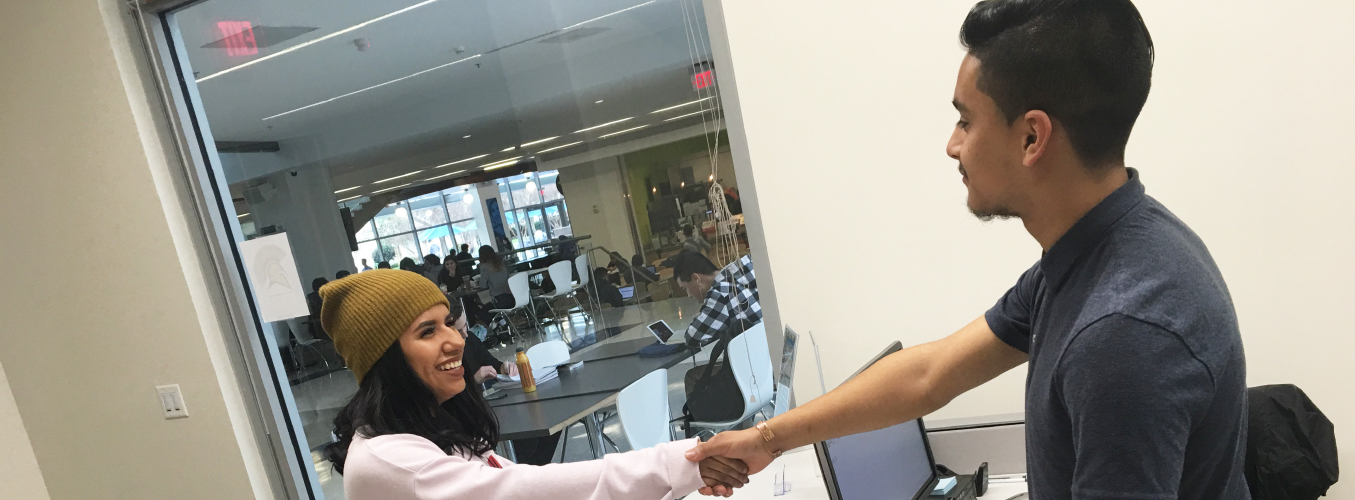 Student shaking hands with person at front desk