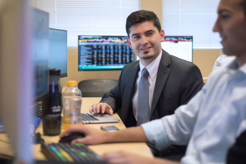 Student in a suit sitting at a desk with a computer.