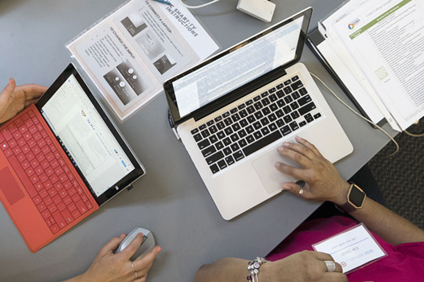 Top view shot of two open laptops on a table with documents.