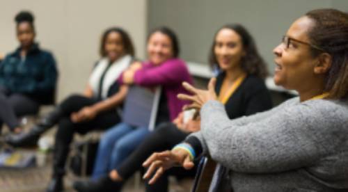 A woman describing something gestering with her arms while three other people in the room pay attention intently.