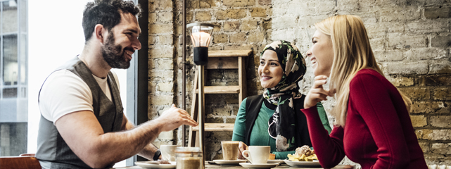 Three people sitting at a table talking and drinking coffee.