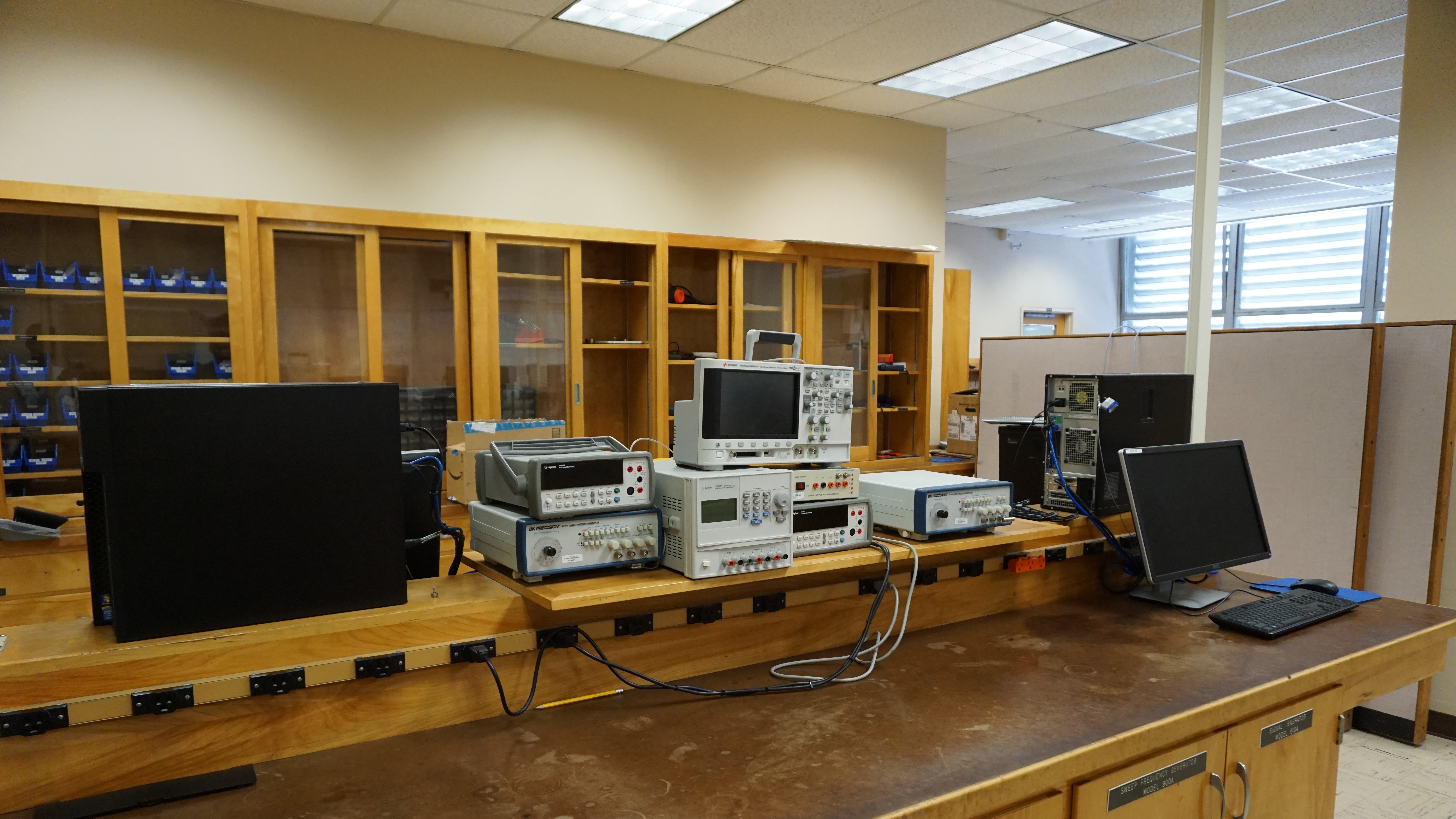 A large wooden counter with computers and electronics. Large shelves are in the background.