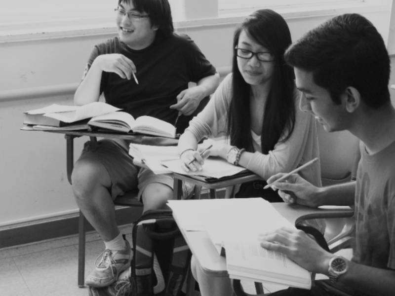 three students sitting at desks and having a discussion