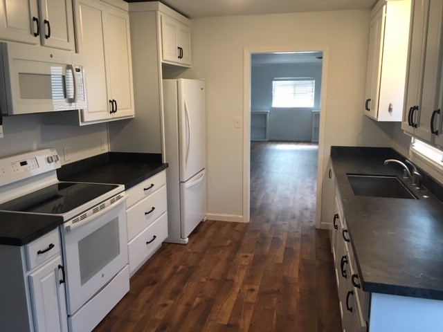 Galley-style kitchen with white cabinets and wood floors