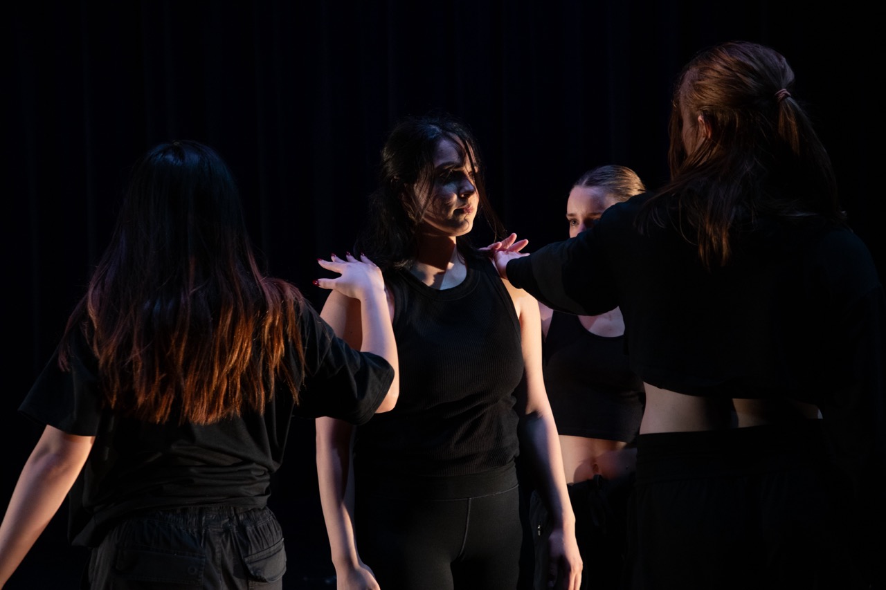 Dancers on stage performing dressed in black.