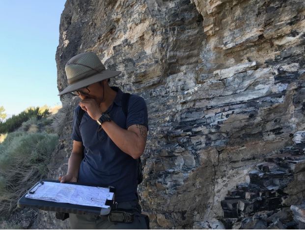 A student standing by a cliff looking at an elevation map on a clipboard