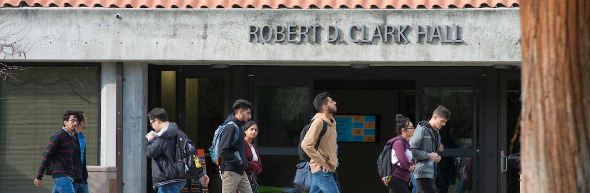 Front of Robert D. Clark Hall entrance with students walking past. 