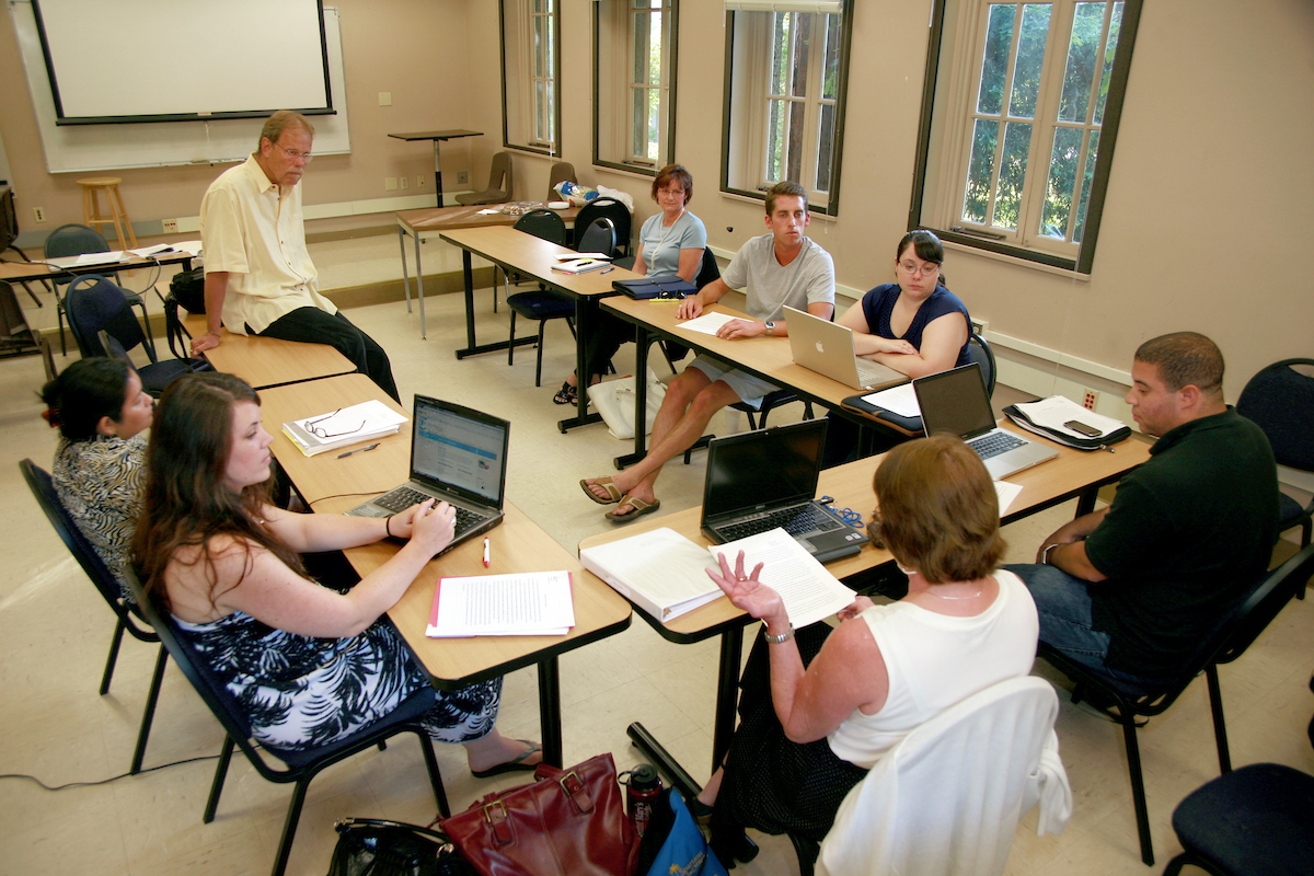 students sitting in a socratic circle with their desks facing each other, talking and gesturing to their computers