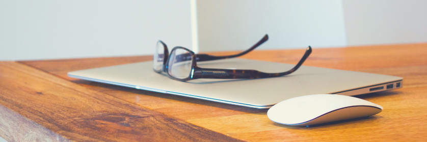 A closed Macbook, Apple mouse, and a pair of glasses.