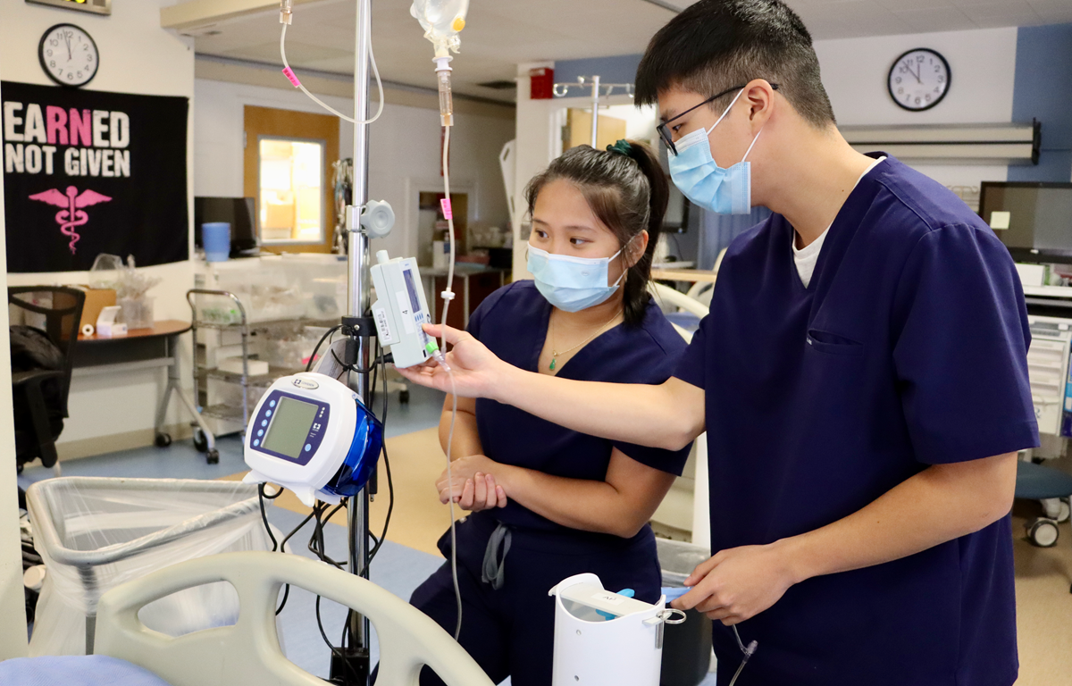 Nursing students in scrubs reading vitals from medical equipment, in the skills lab.