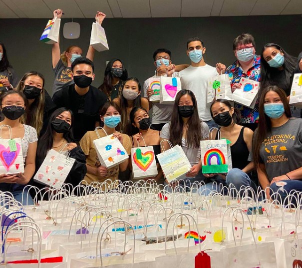 A large group of CNSA members, indoors, wearing masks, posing with decorated bags during a volunteer event.