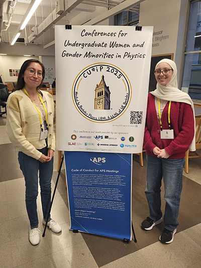 Photograph of Emily Foreman and Mariana Rojas-Montoya standing in front of a CU*iP poster.