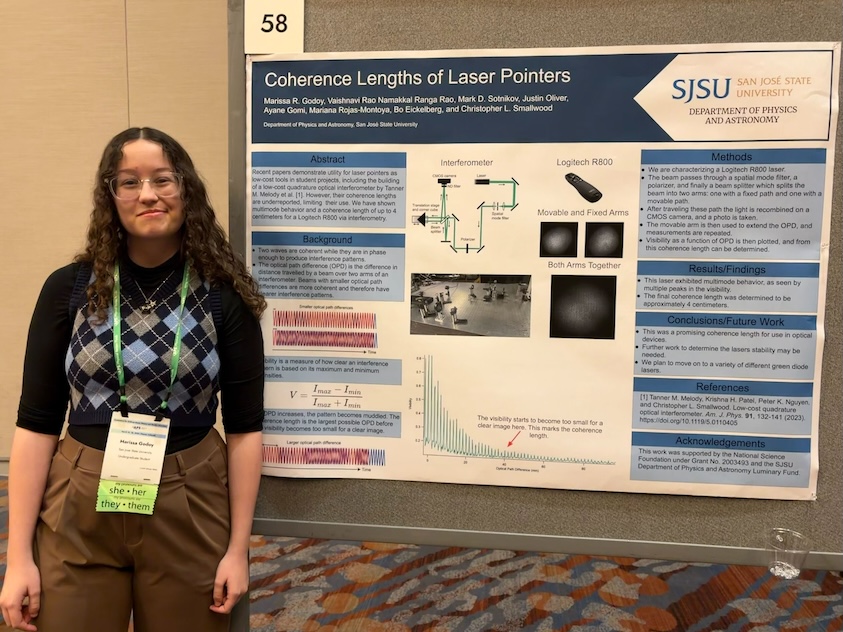 Photograph of Marissa Godoy standing in front of a physics poster.