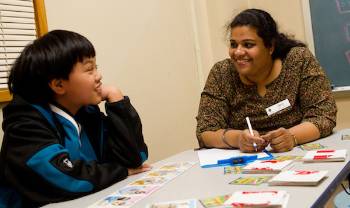 teacher sits at low table with child.  activity materials scattered on table, they're both smiling