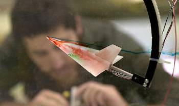 a model plane with colored coming off it is seen in foreground, person bending over concentrating in back