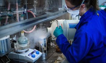 woman pours steaming vessel into smaller container under fume hood