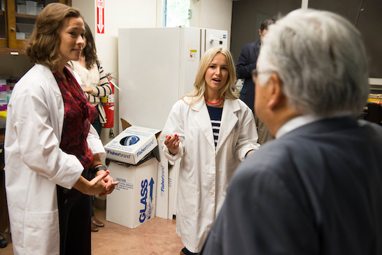 two people in lab coats talk to visitor in lab