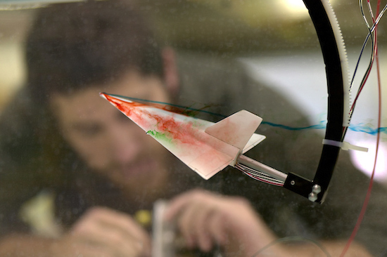 closeup of airplane shape test with colored smoke streaming from wings. blurred person in background