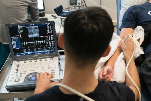 looking over a person's shoulder as they hold a sensor to a subject's arm and look at a readout on screen