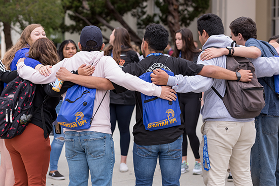 students with sjsu branded items stand in a big group hug