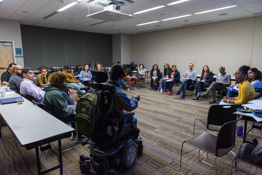 a group of approximately 20 people of various backgrounds and abilities sitting in chairs in a circle engaged in conversation