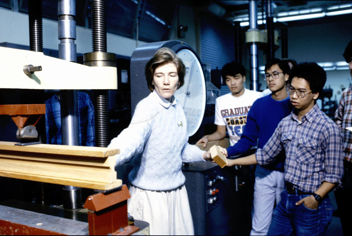 Thalia showing students a wood beam in a lab.